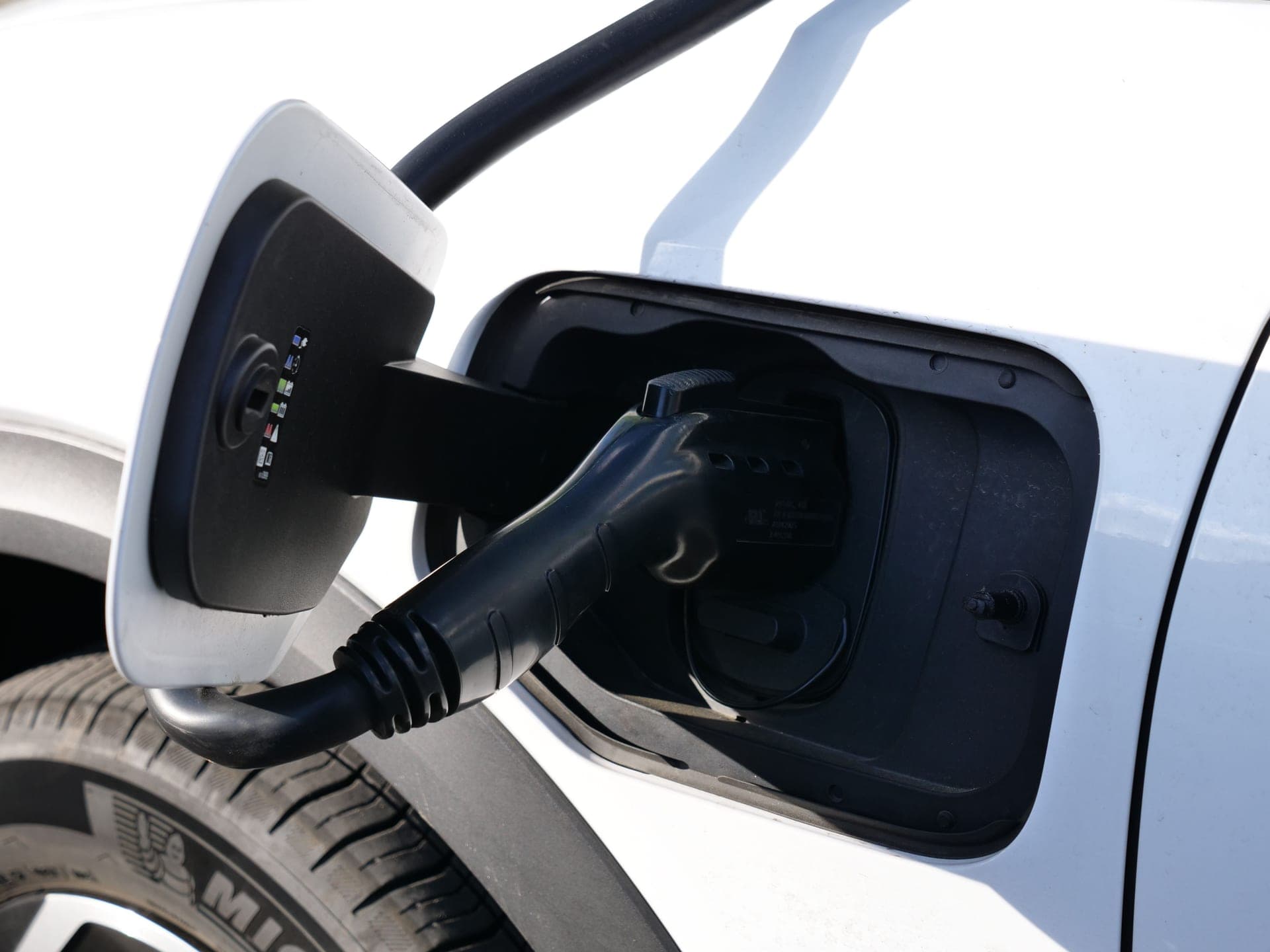 Close-up of an EV charging connector plugged into a vehicle charge port in sunlight